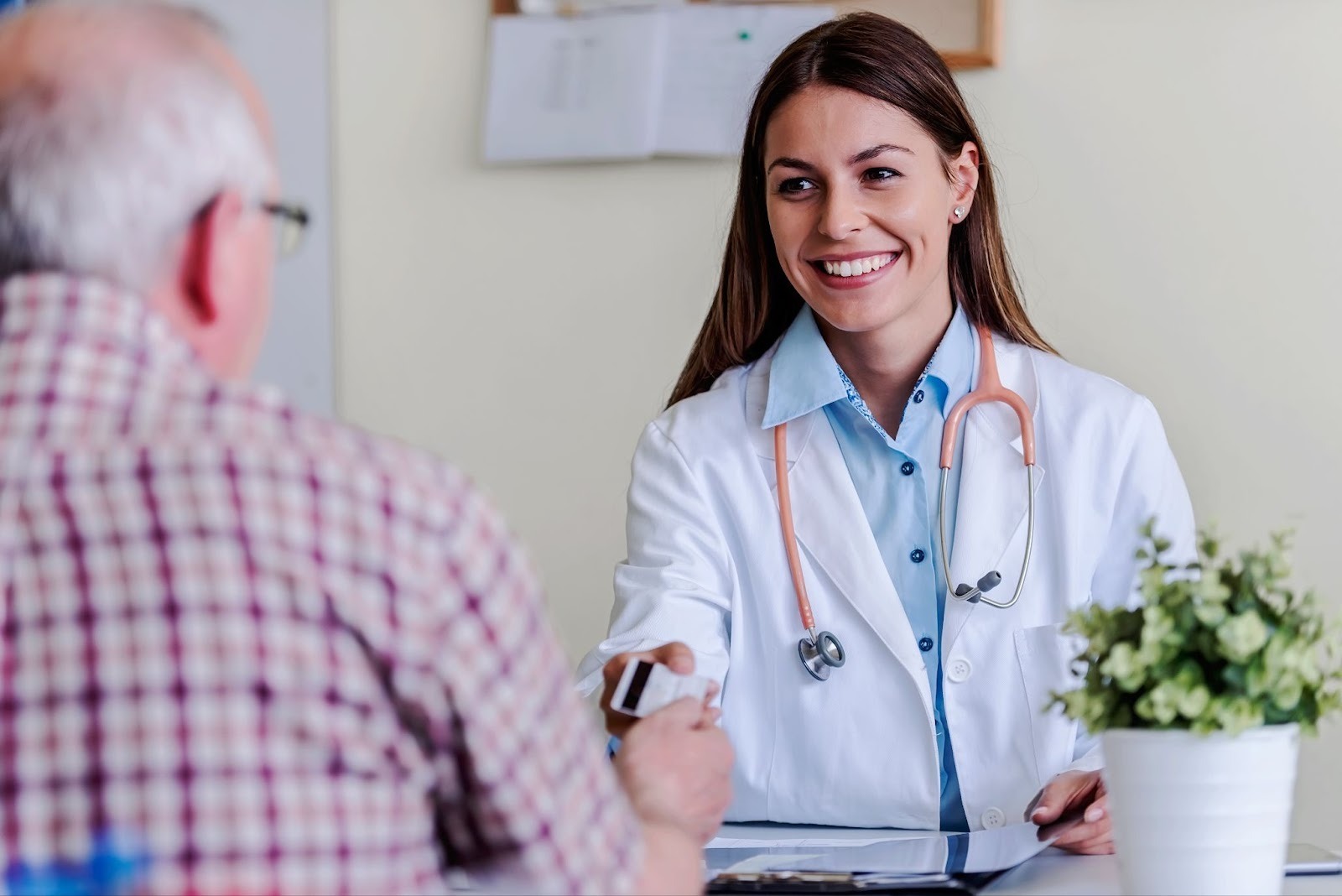 Smiling female orthodontist in white coat with stethoscope shaking hands with male patient in plaid shirt, discussing braces options at White Orthodontics in Eagle Mountain.