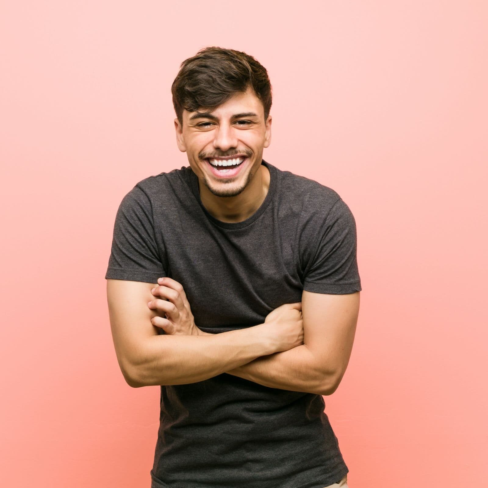 Smiling man with crossed arms against a pink background, reflecting confidence and self-love, relevant to White Orthodontics' mission of enhancing smiles and personal well-being.