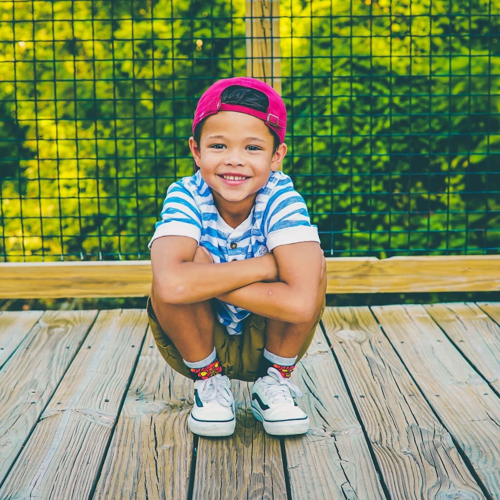 Smiling boy in a striped shirt and cap, sitting on wooden deck, showcasing a confident smile and relaxed posture, reflecting the joy of orthodontic care at White Orthodontics.