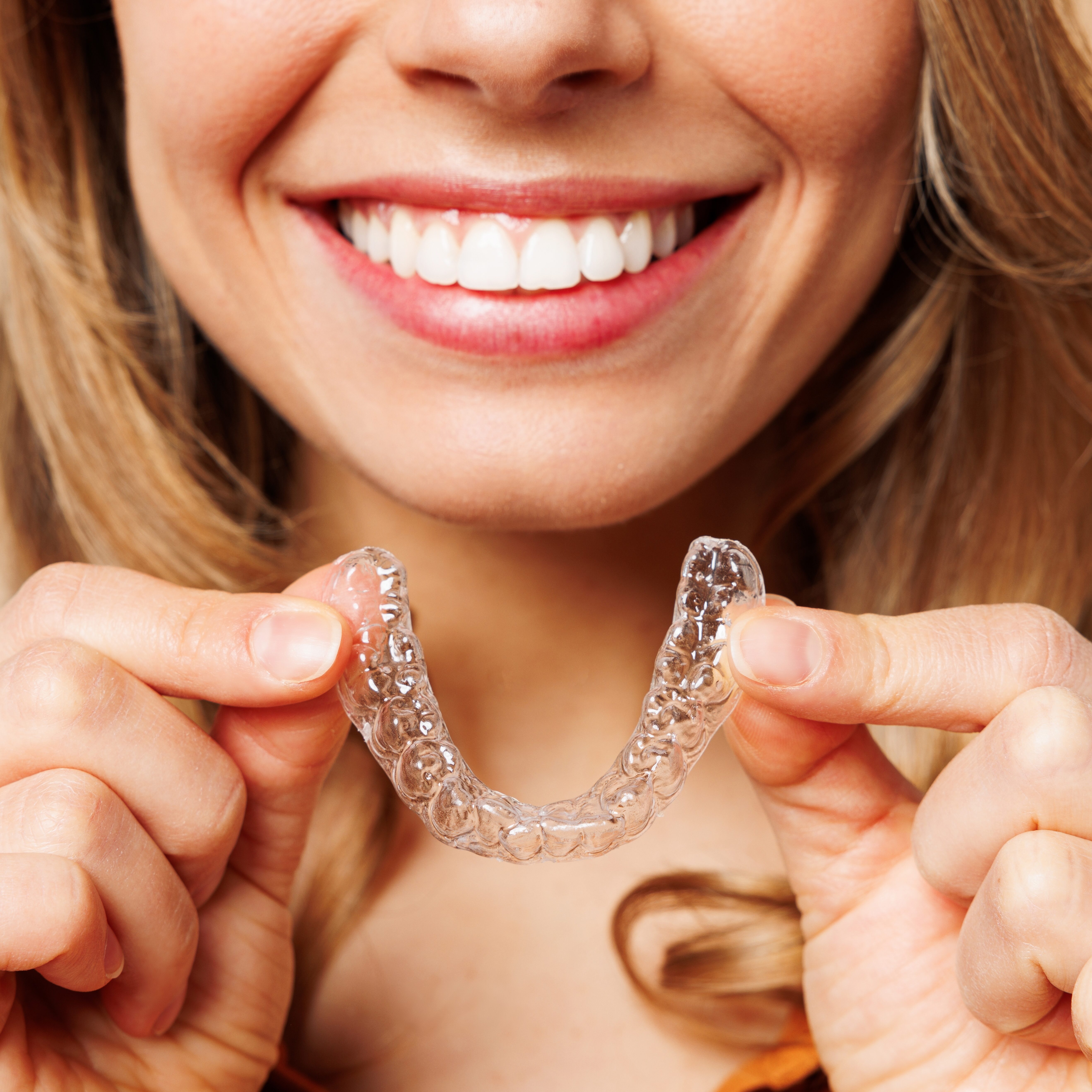 Smiling woman holding clear Invisalign aligner, showcasing orthodontic treatment option for straighter teeth.
